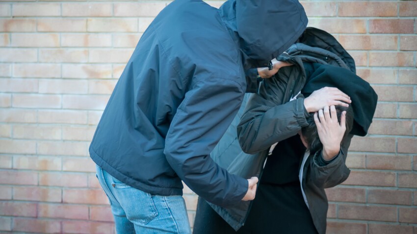 Bullying, aggression and violence scene between two males, one young adult male punches his peer near a bricks wall